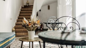 A staircase leading to a second floor, a round table with a metal frame, and a vase with dried flowers on a small stool. - Riad NayaNour (Marrakech)
