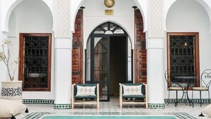An entrance with two wooden doors, a central archway, and a seating area with two chairs and a table. - Riad NayaNour (Marrakech)