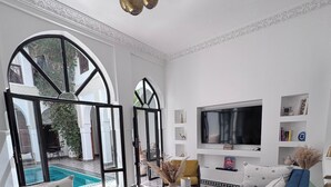 A living room with two blue sofas, a TV, and a pool view. - Riad NayaNour (Marrakech)