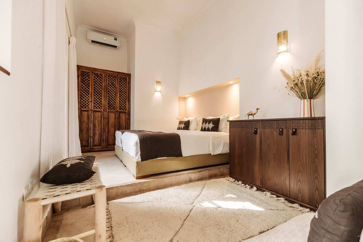 A bedroom with a bed, wooden wardrobe, and a small seating area.