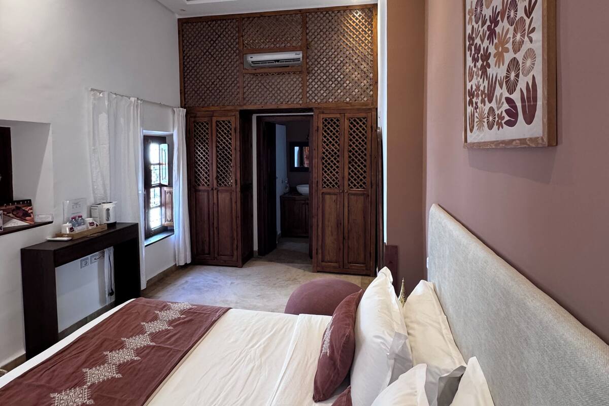 A spacious bedroom with a large bed, a desk with toiletries, a decorative wall piece, and a view to a balcony.