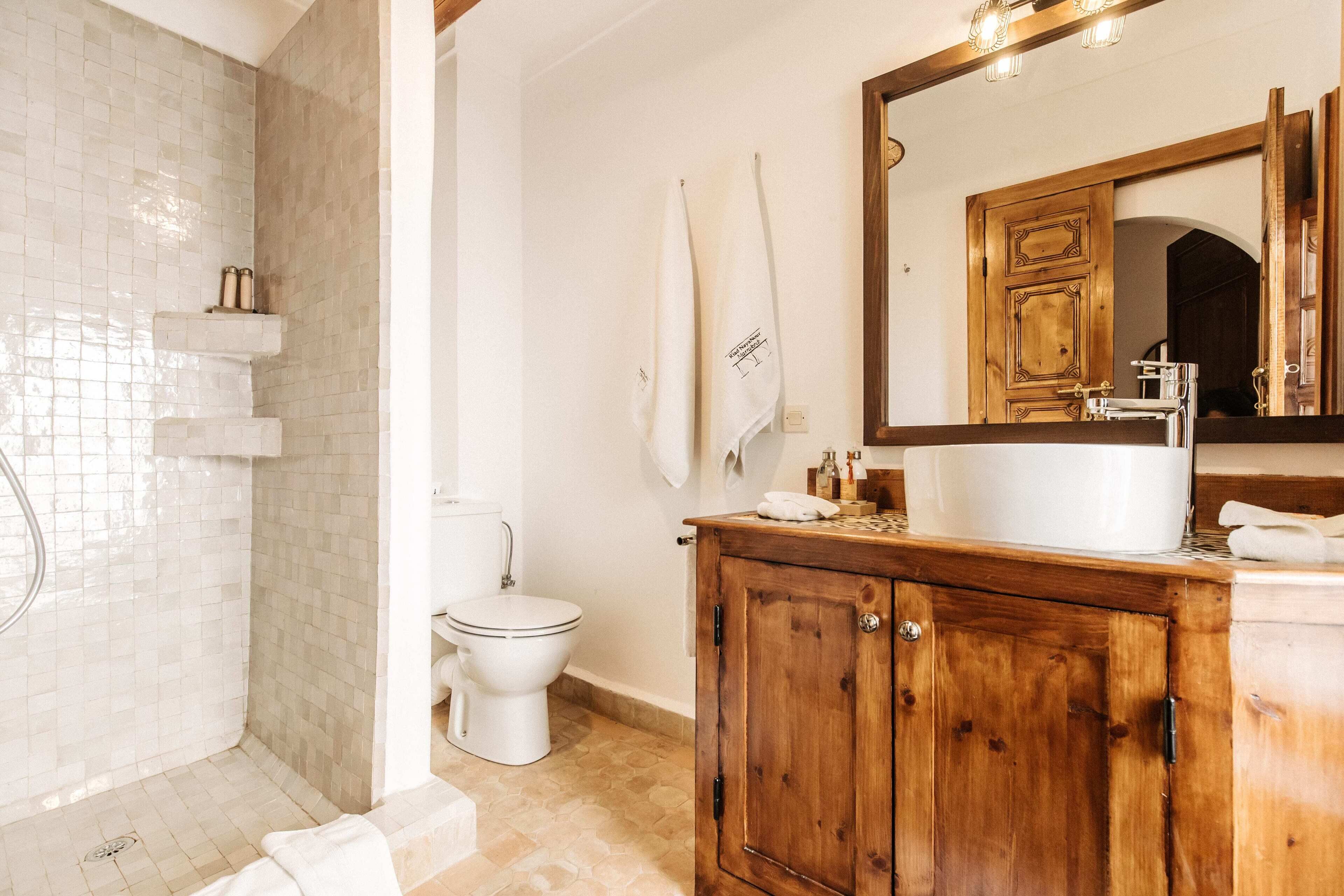 A bathroom with a shower, toilet, wooden vanity, and a large mirror.