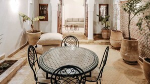 A courtyard with a round table and chairs, potted plants, and a view of a room with a sofa and a window. - Riad NayaNour (Marrakech)