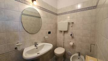 A bathroom with a round mirror, a sink, a toilet, and a bidet.