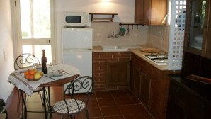 A compact kitchen with a refrigerator, microwave, sink, and a gas stove. There's a dining table with chairs and a bottle of wine.