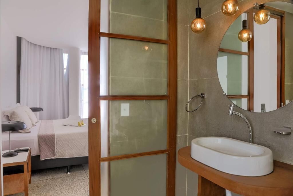 A hotel room with a bed, bedside table, and a bathroom with a sink and mirror.