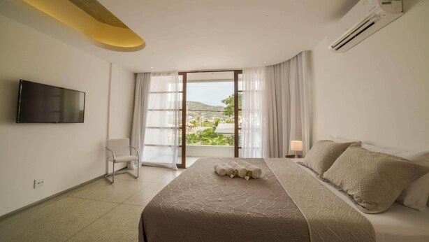 Una habitación de hotel con cama, televisor, sillón y ventana con cortinas.