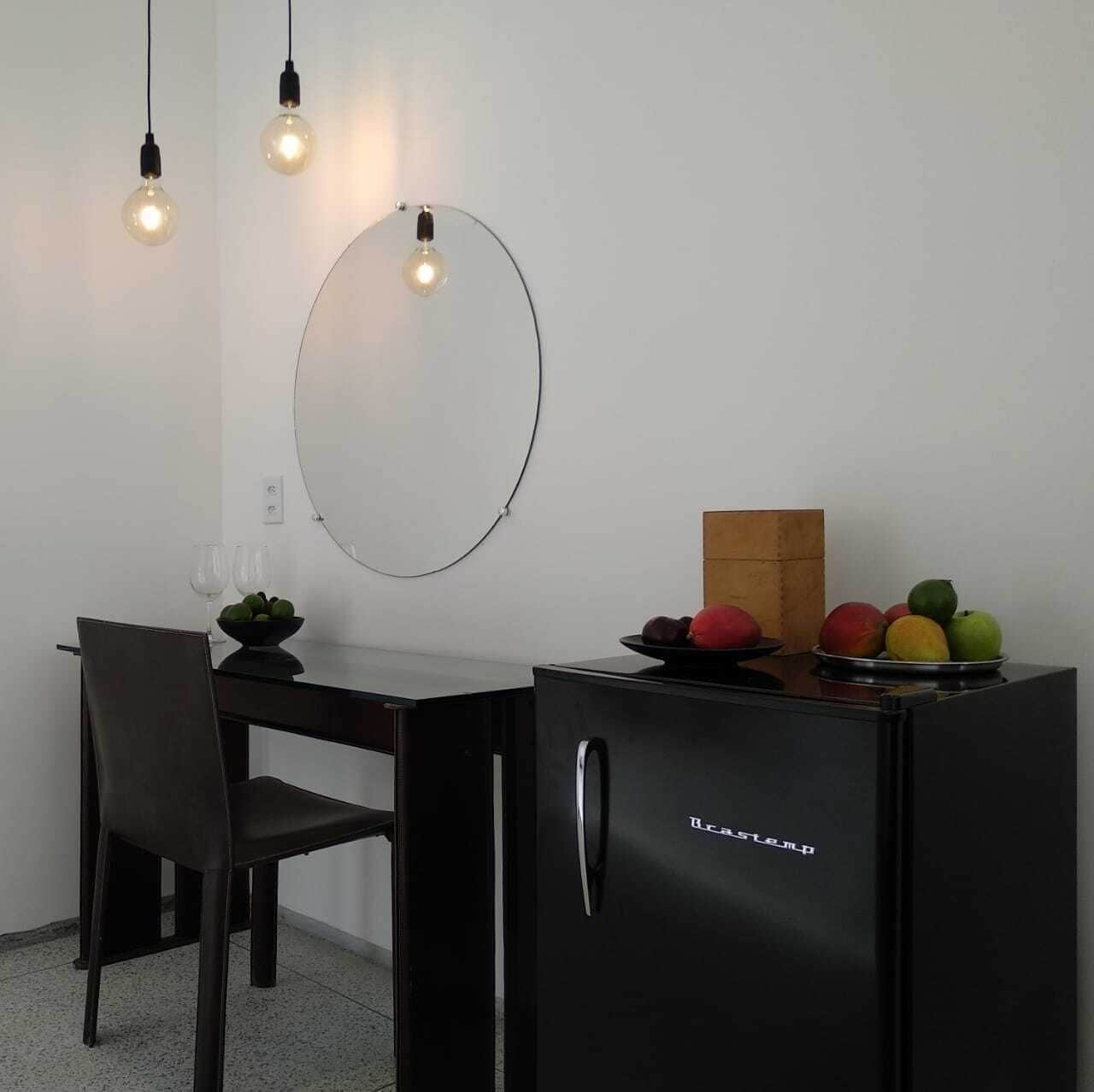 Una cocina compacta con refrigerador, una mesa de comedor con sillas y un frutero sobre la encimera.