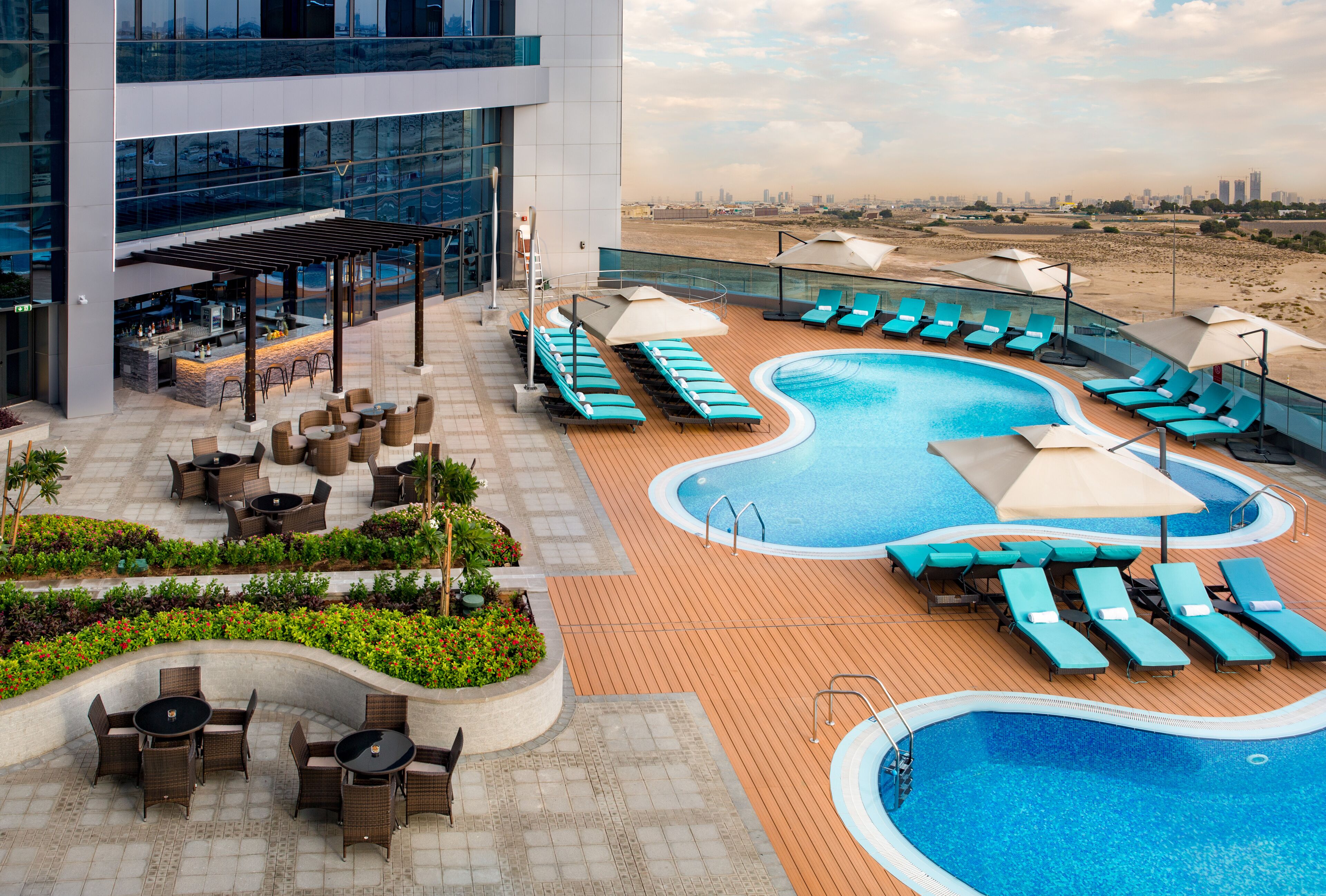 Un espace piscine aménagé sur le toit, avec des chaises longues, un bar et une vue sur le panorama urbain.