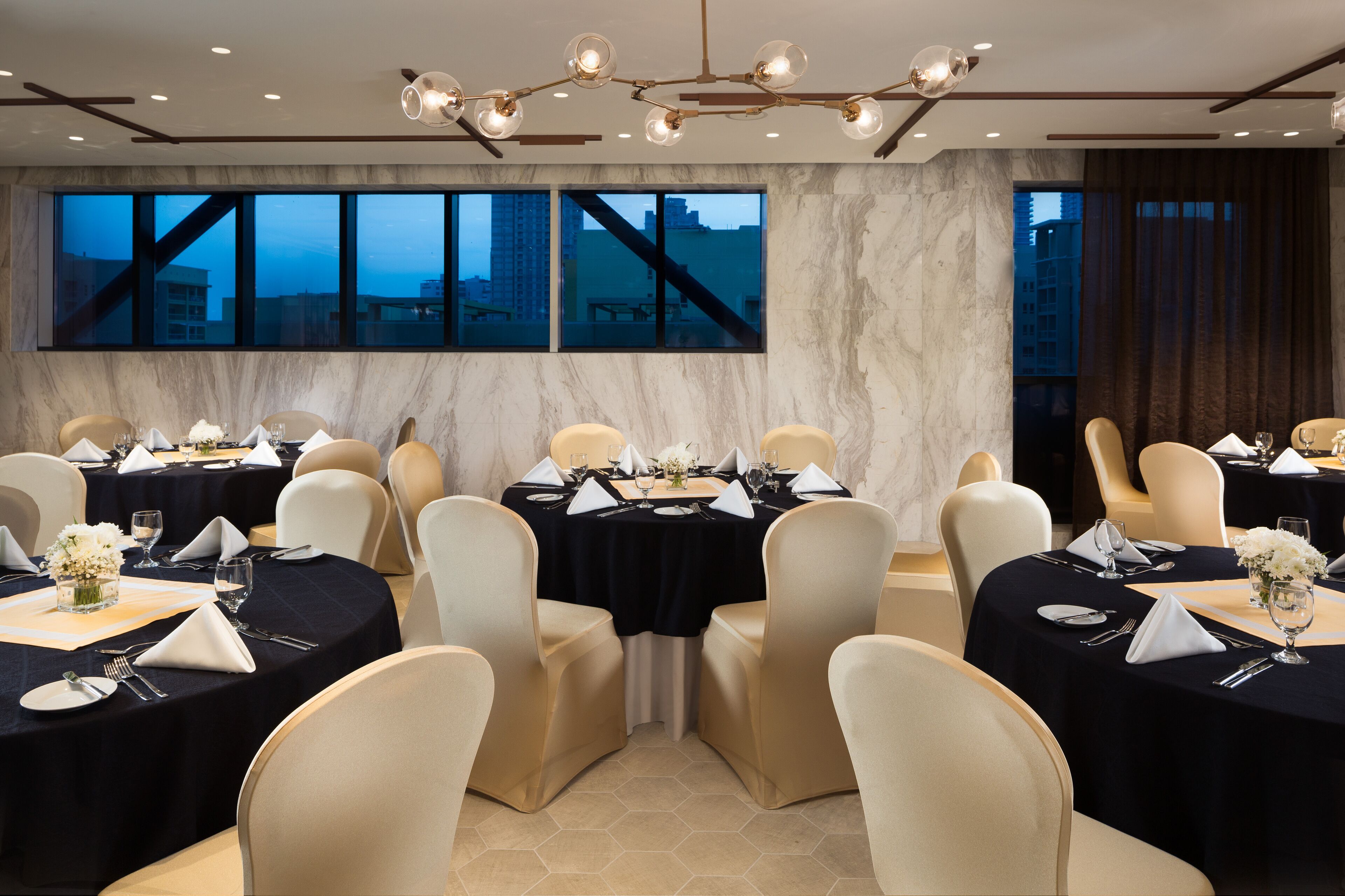 A dining area with round tables, beige chairs, and black tablecloths.