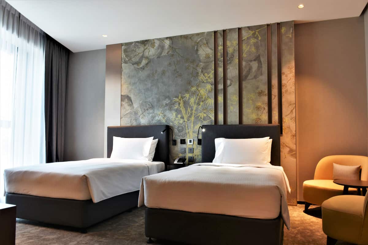 Habitación de hotel con dos camas, un sofá, una mesita pequeña y un cuadro abstracto grande en la pared.