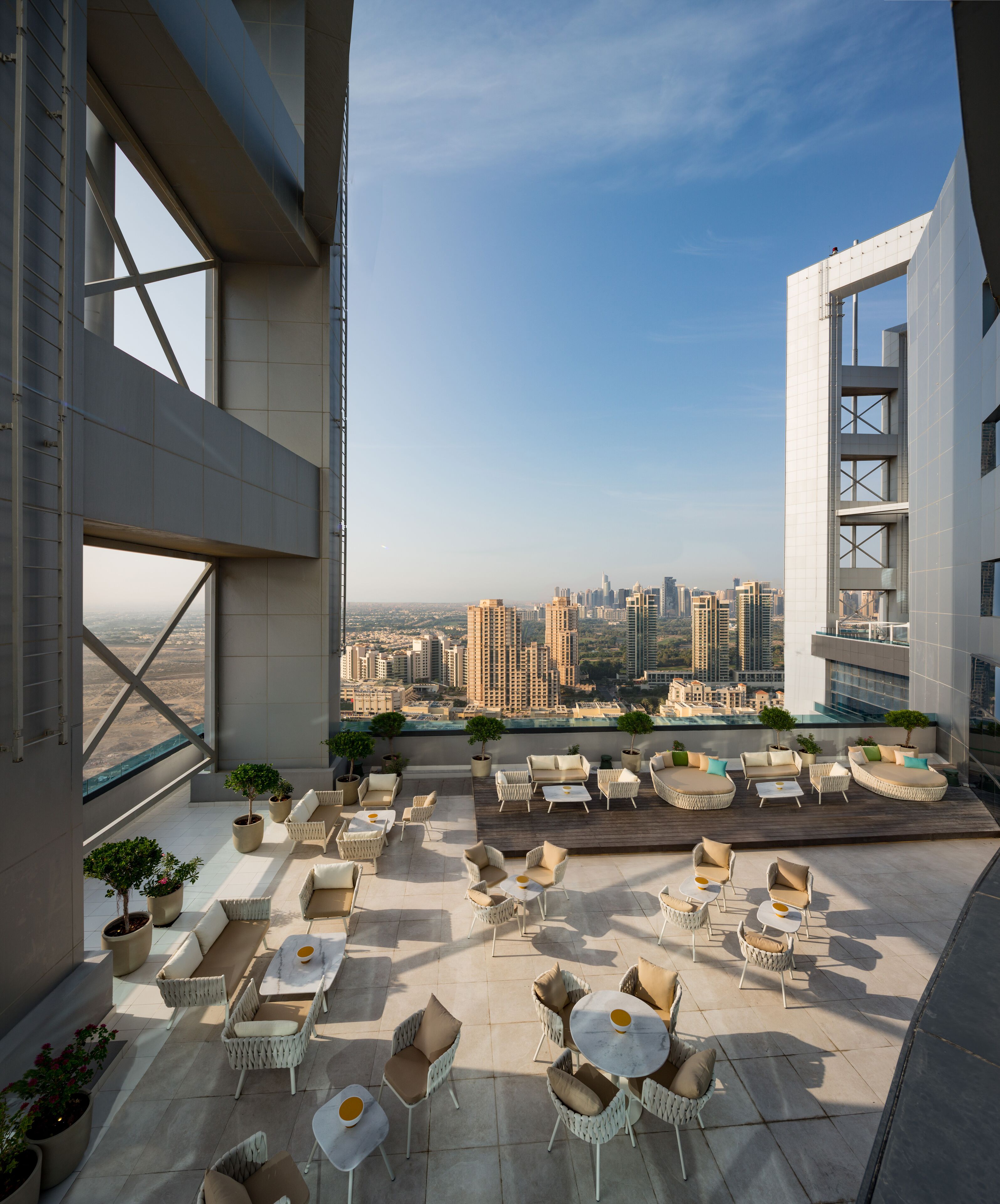 A rooftop terrace with outdoor seating, potted plants, and a cityscape view.