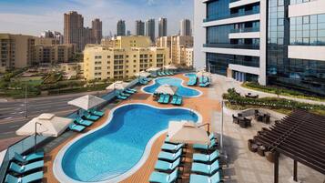 A rooftop swimming pool with lounge chairs and umbrellas, surrounded by modern buildings and a cityscape.