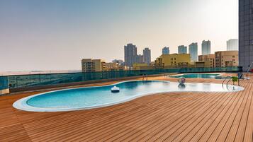 Enjoy a refreshing swim with a city view from our rooftop pool, surrounded by lounge chairs and a poolside table.