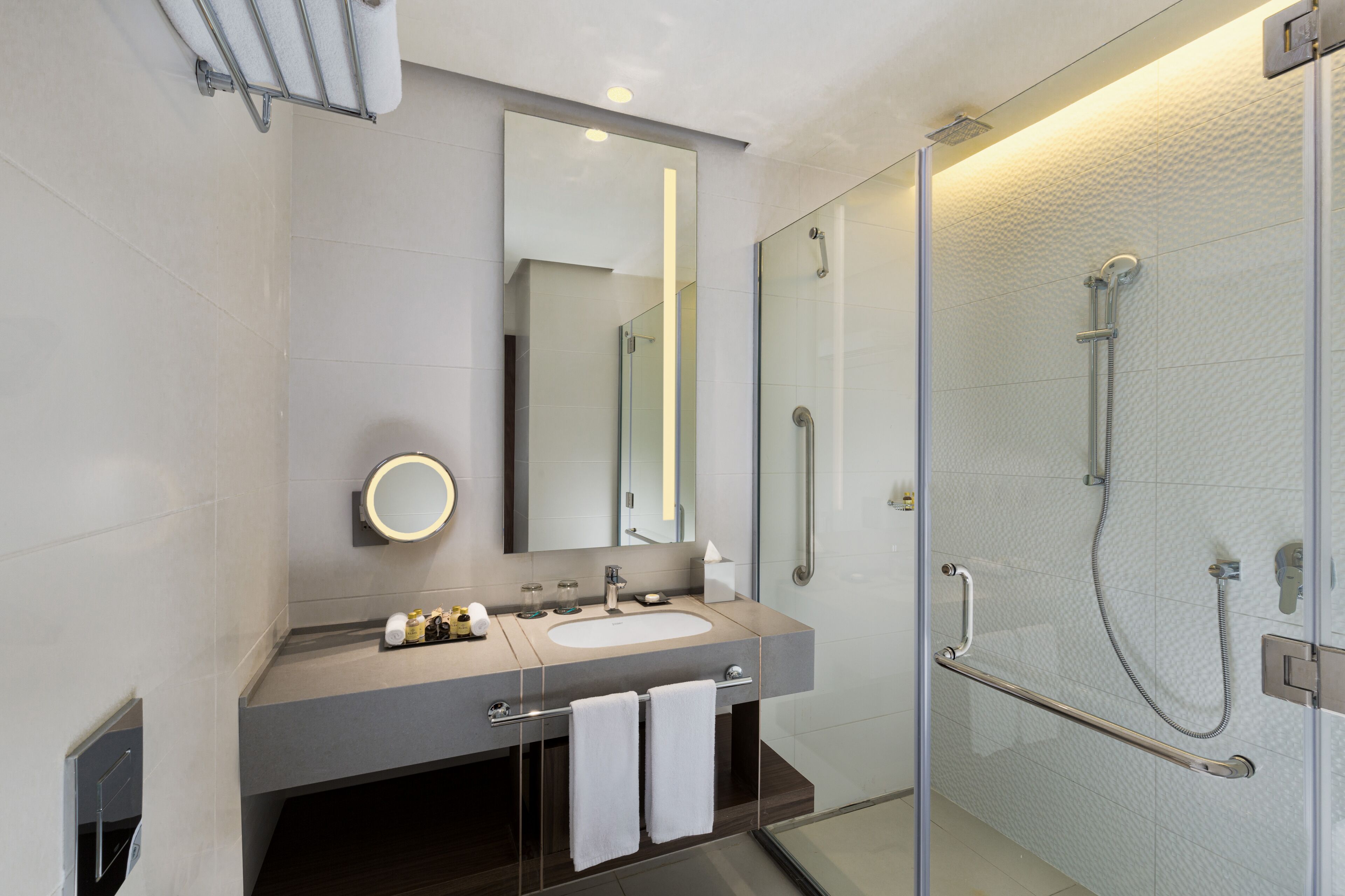 Un baño moderno con ducha envuelta en vidrio, un espejo grande y tocador con lavabo y perchero para toallas.