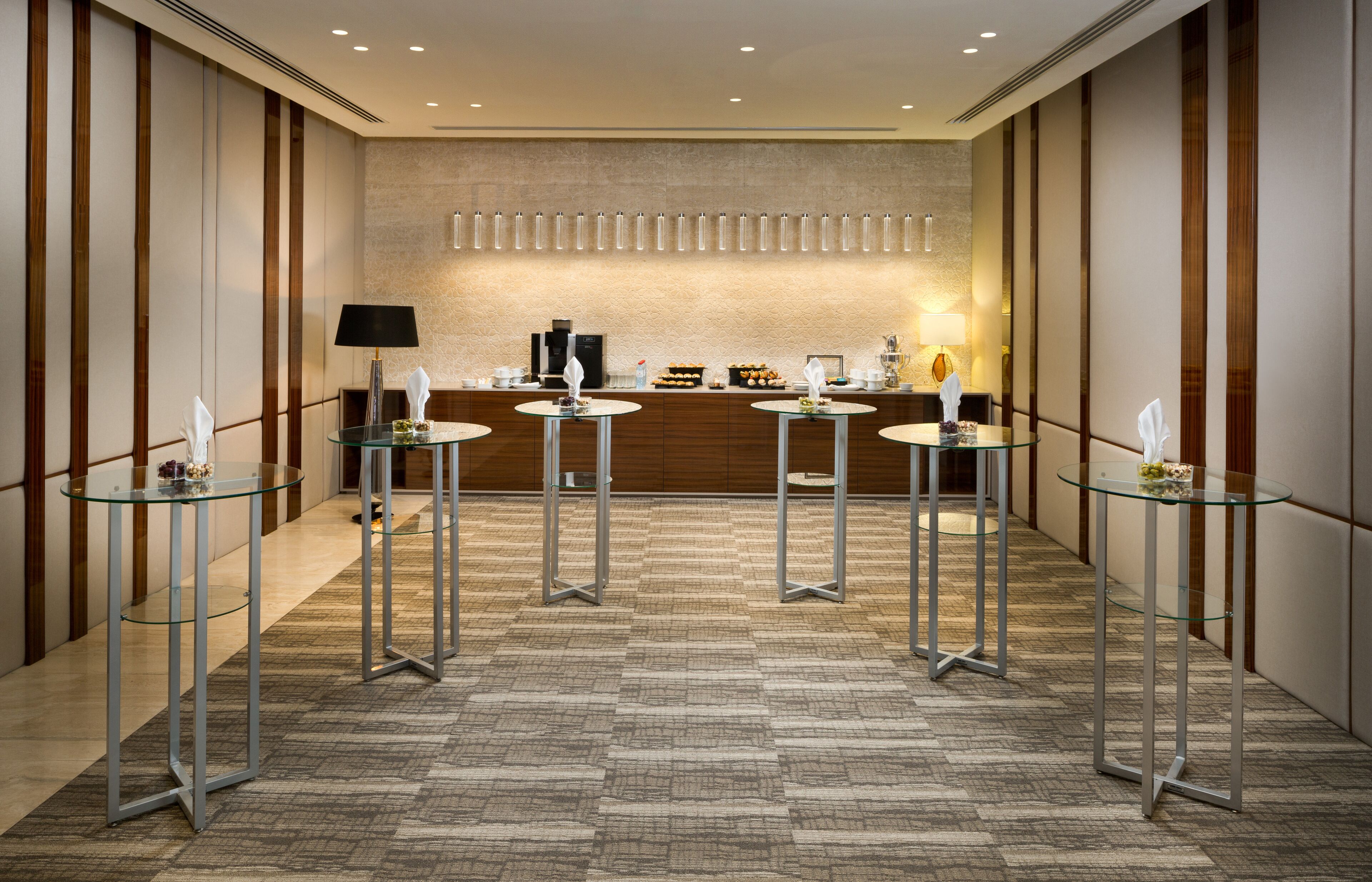 A modern hotel lobby with a reception desk, glass tables, and a patterned carpet.