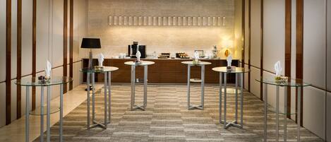 A modern hotel lobby with a reception desk, glass tables, and a patterned carpet.