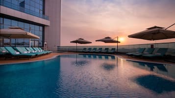 A swimming pool with lounge chairs and umbrellas, surrounded by a modern building with large windows.