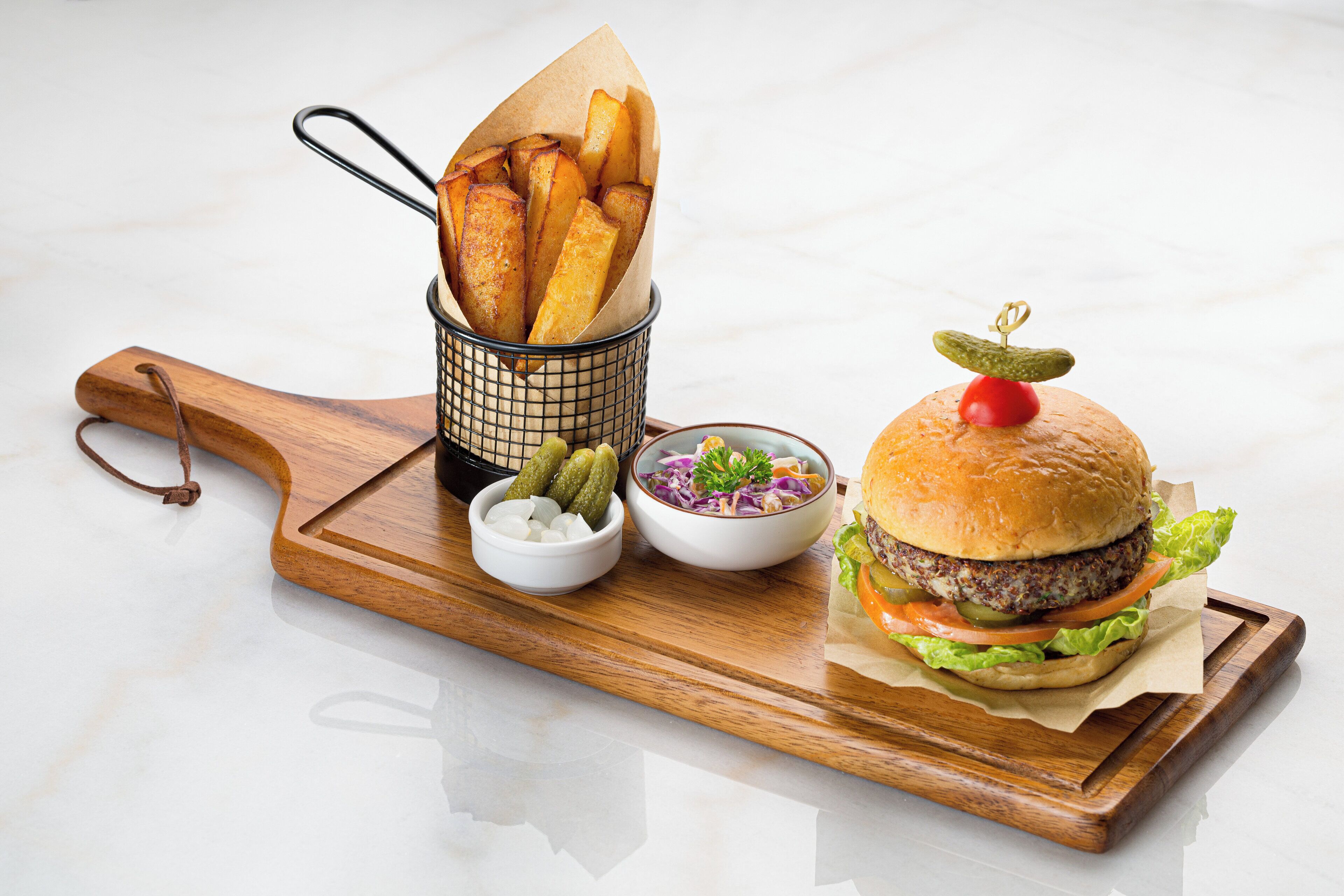 A wooden serving board with a burger, fries, and a side salad.