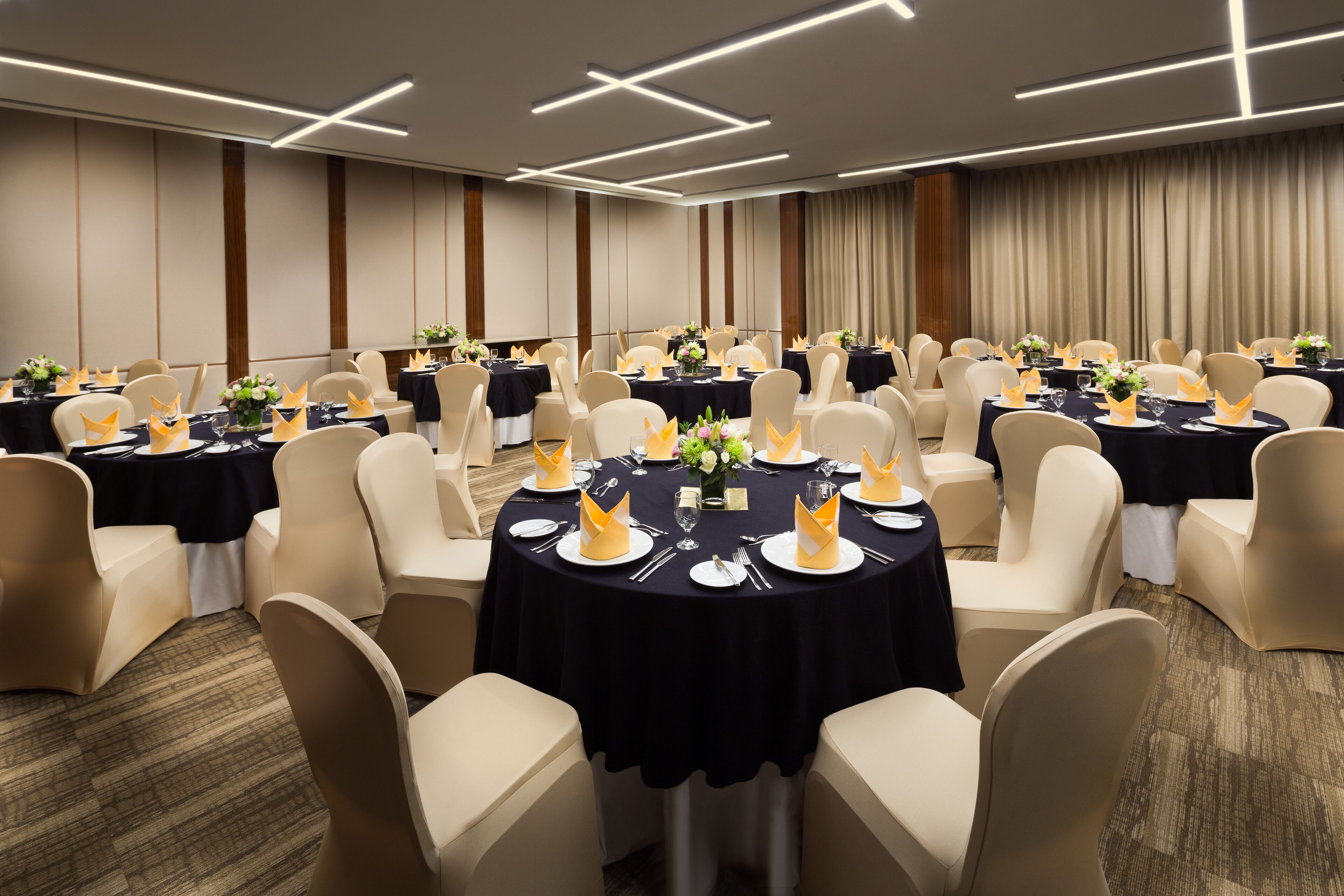 Une salle de banquet avec des tables rondes recouvertes de nappes noires, des chaises blanches et des serviettes jaunes.