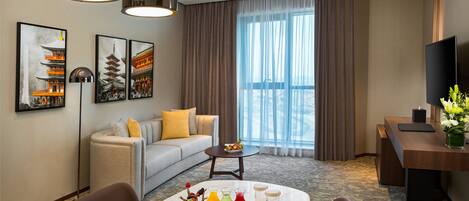 Une chambre d’hôtel comprenant un coin repas, un canapé, une télévision et des œuvres d’art aux murs.