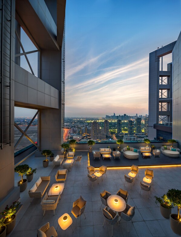 A rooftop terrace with outdoor seating, potted plants, and a cityscape view.