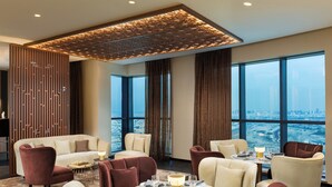 Un comedor moderno con vistas a la ciudad, que presenta una combinación de sillas rojas y beiges, una mesa redonda y un panel decorativo en el techo.