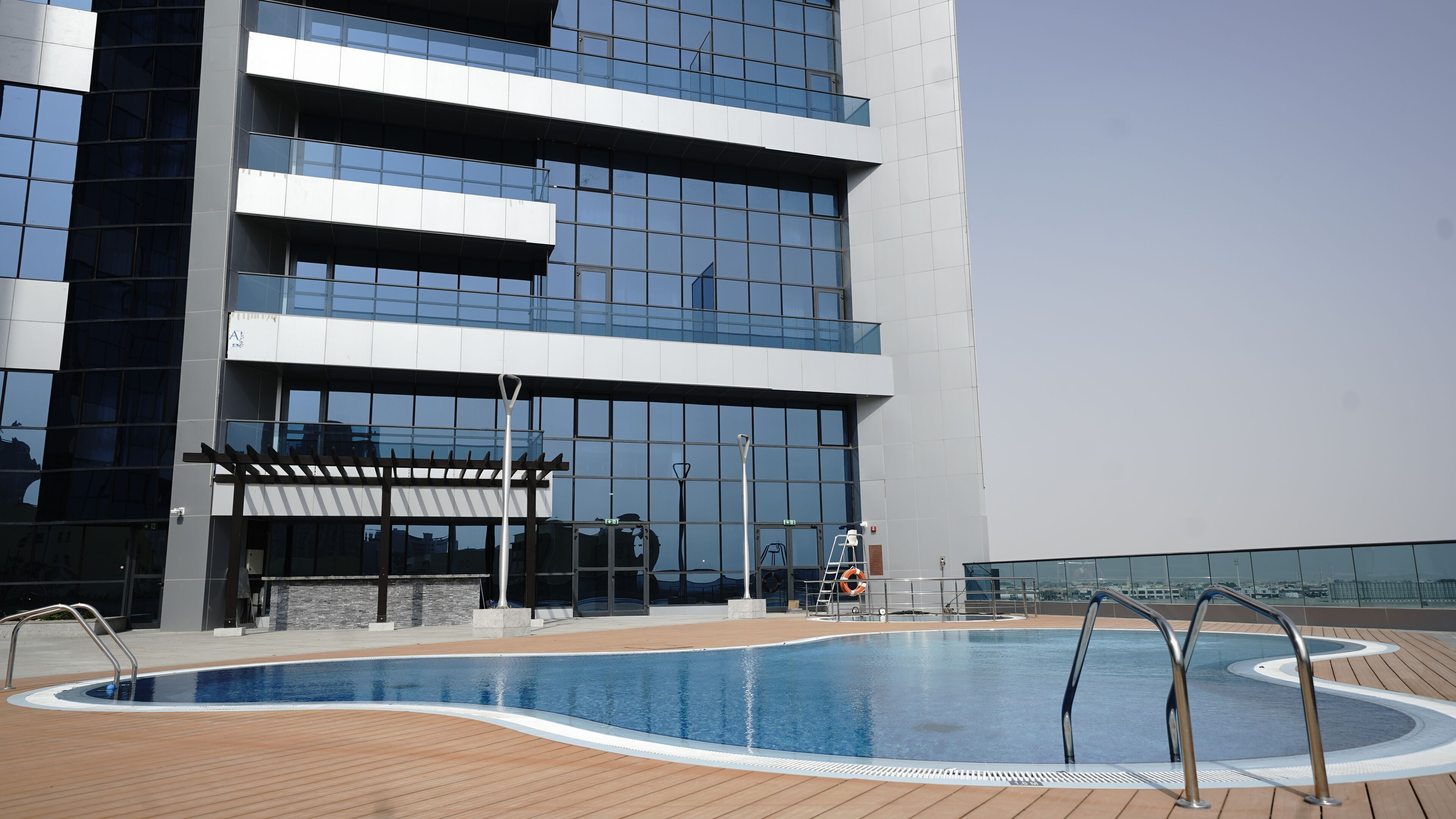 A modern building with a rooftop pool, large windows, and a covered seating area.