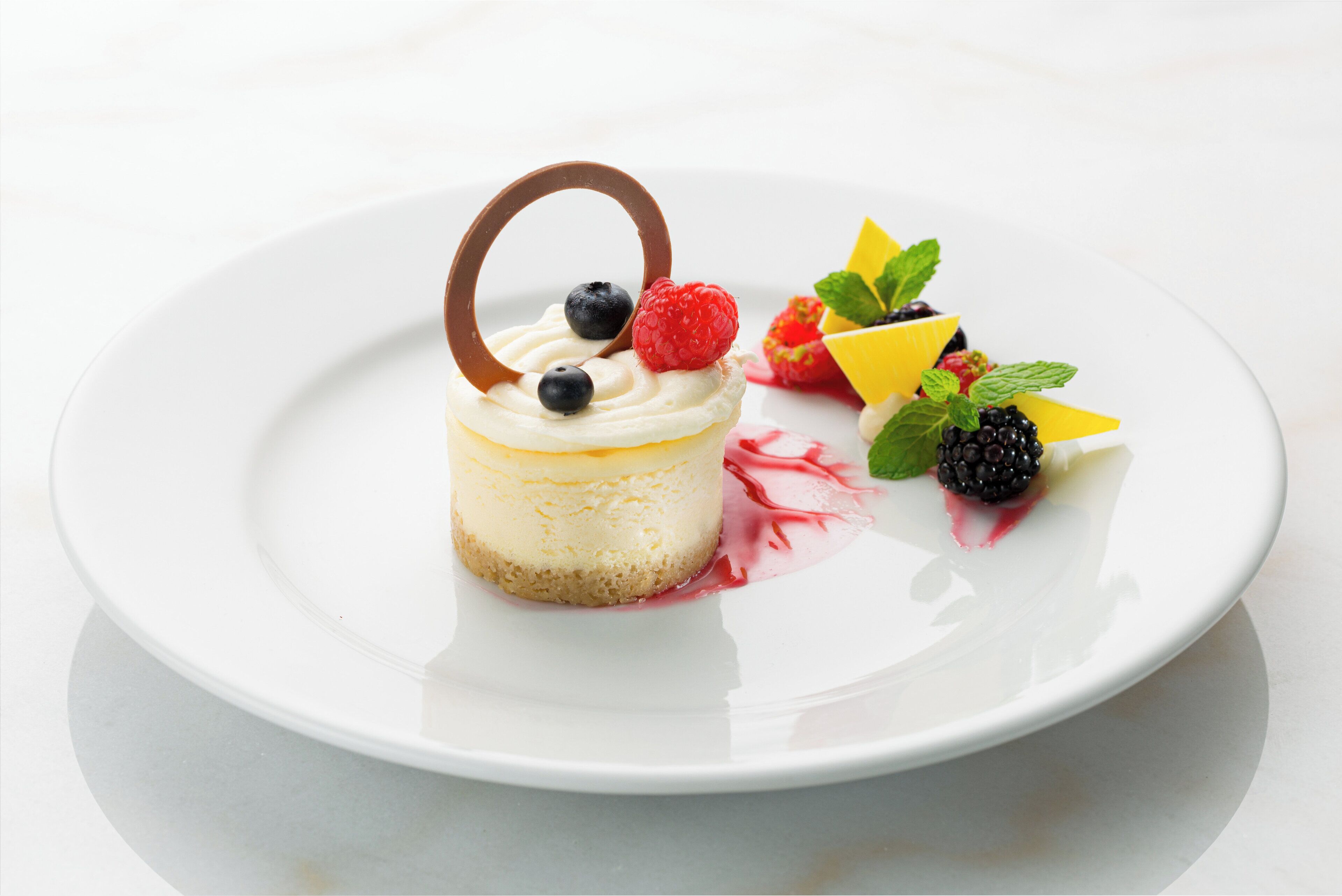 A dessert on a white plate with a handle, topped with blueberries, raspberries, and blackberries, and garnished with mint leaves.