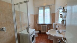 A bathroom with a glass shower enclosure, a washing machine, a toilet, a radiator, and a sink. - Affittacamere Residenza Chiara (Forlì)