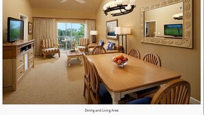 Un espace repas et un salon comprenant une grande table, des chaises, un téléviseur et un ventilateur de plafond.