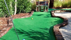 Un parcours de mini-golf avec un tapis vert pour les putts, un club de golf jaune et une balle de golf bleue.