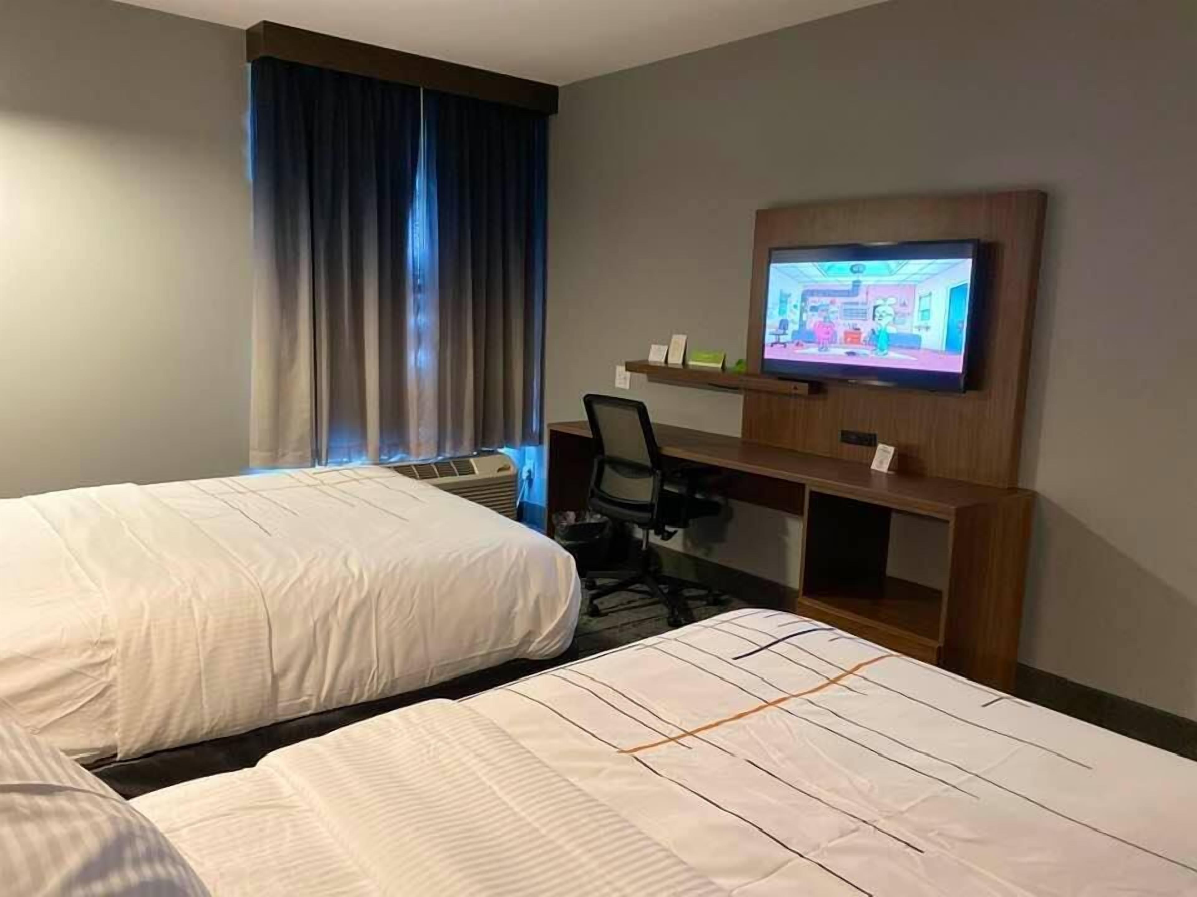 A hotel room with two beds, a desk, a television, and a window with curtains.