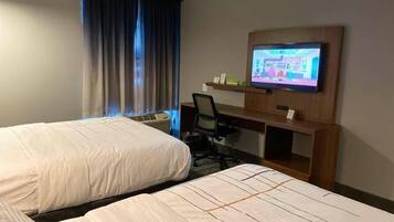 A hotel room with two beds, a desk, a television, and a window with curtains.