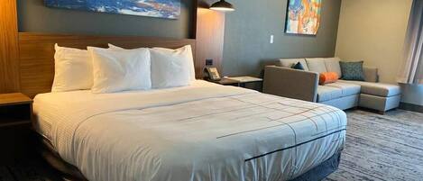 A hotel room with a large bed, a sofa, and two paintings on the walls.