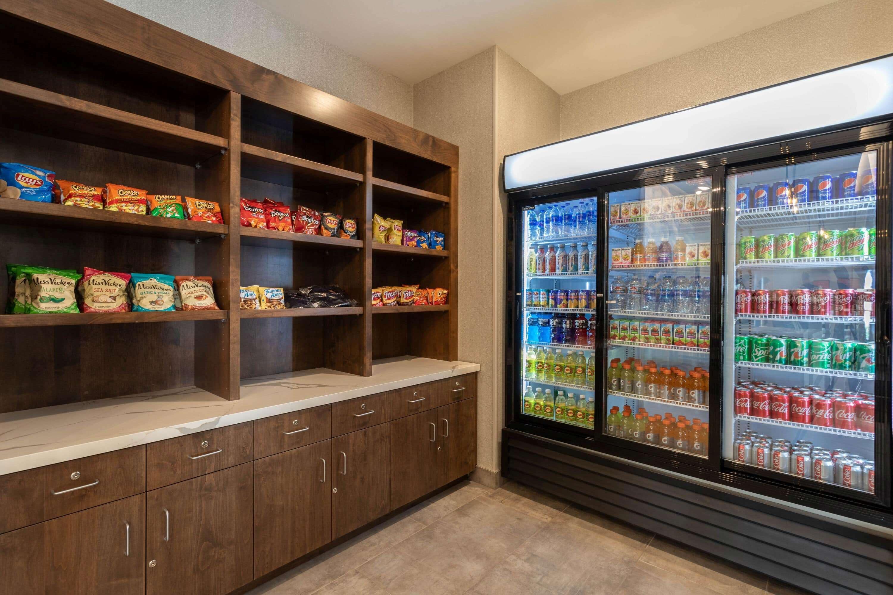 A snack bar with shelves of chips and a beverage refrigerator stocked with sodas and juices.