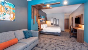 Una habitación de hotel moderna con un sofá gris, una cama, un escritorio y un televisor.