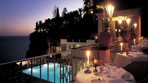 A rooftop dining area with tables set for dinner, overlooking a pool and the ocean.
