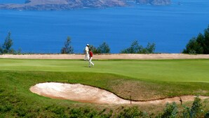 A golf course with a view of the ocean and rocky cliffs in the background.