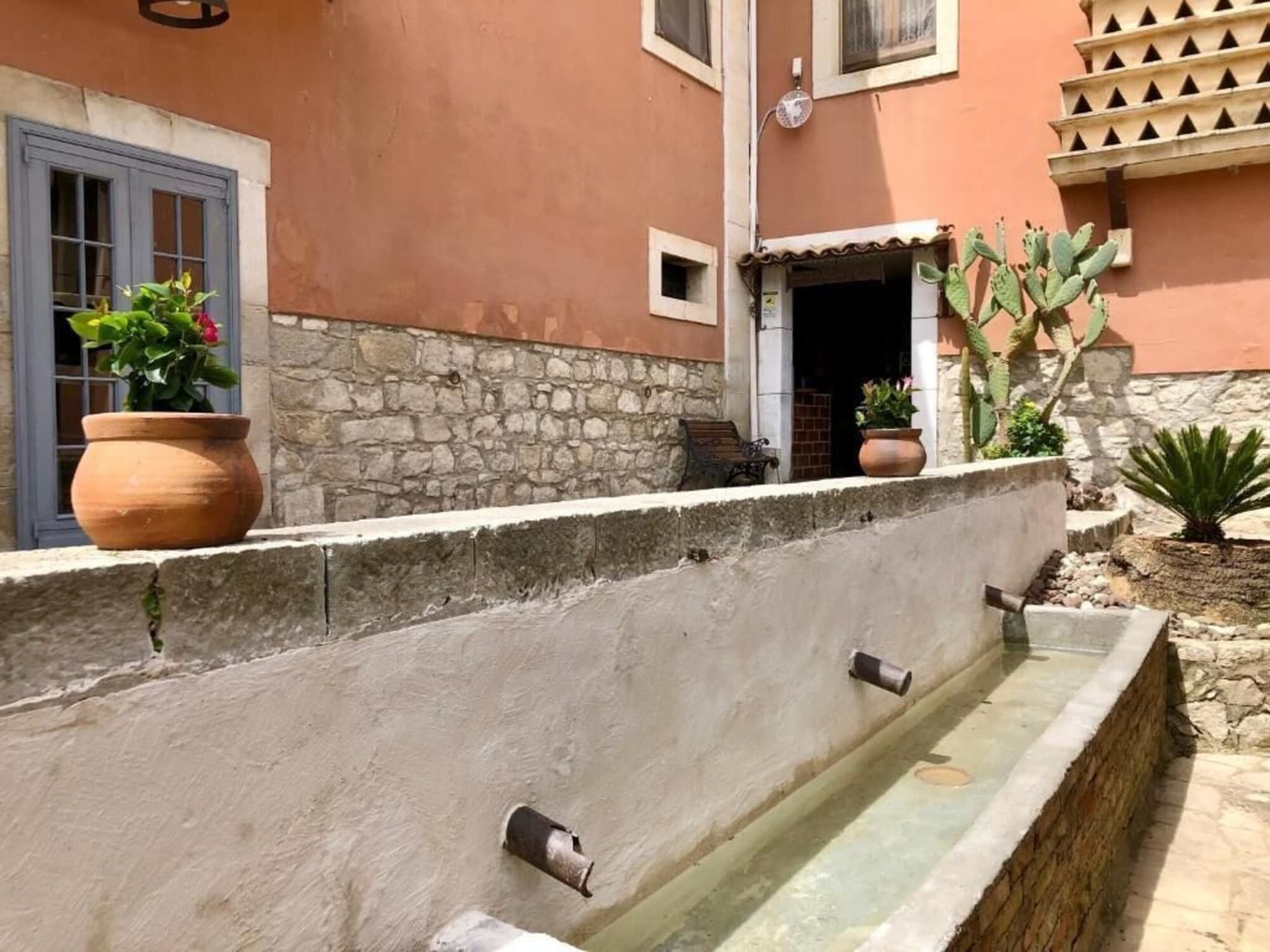 Une cour intérieure avec un mur en pierre, un élément décoratif aquatique et des plantes en pot.