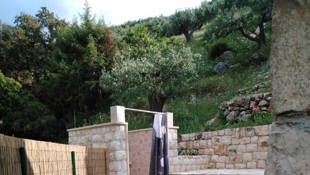A stone-walled outdoor area with a stone bench and a hanging shower curtain. - Lovrečina sand beach (Postira)