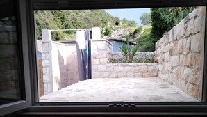 A view through a window of a stone-walled outdoor area with a pool and greenery. - Lovrečina sand beach (Postira)