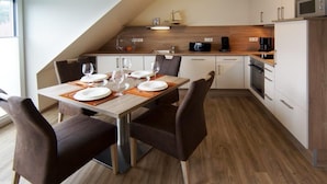 Une cuisine moderne avec un coin repas, comprenant une table en bois pour quatre personnes, des chaises foncées et un four encastré.