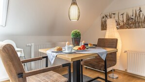 Un coin repas avec une table dressée pour deux personnes, une plante en pot et un tableau accroché au mur.