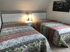 Ein Schlafzimmer mit zwei Betten, jeweils mit einem gemusterten Überwurf, einem Nachttisch mit Lampe und einem Wandbild.