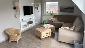 Ein modernes Wohnzimmer mit Flachbildfernseher, einer Couch, einem Couchtisch und einem Korbstuhl.