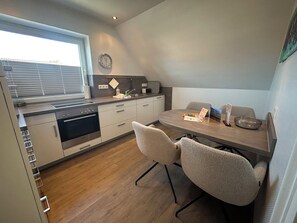 A modern kitchen with a dining area, wooden flooring, and a clock on the wall.