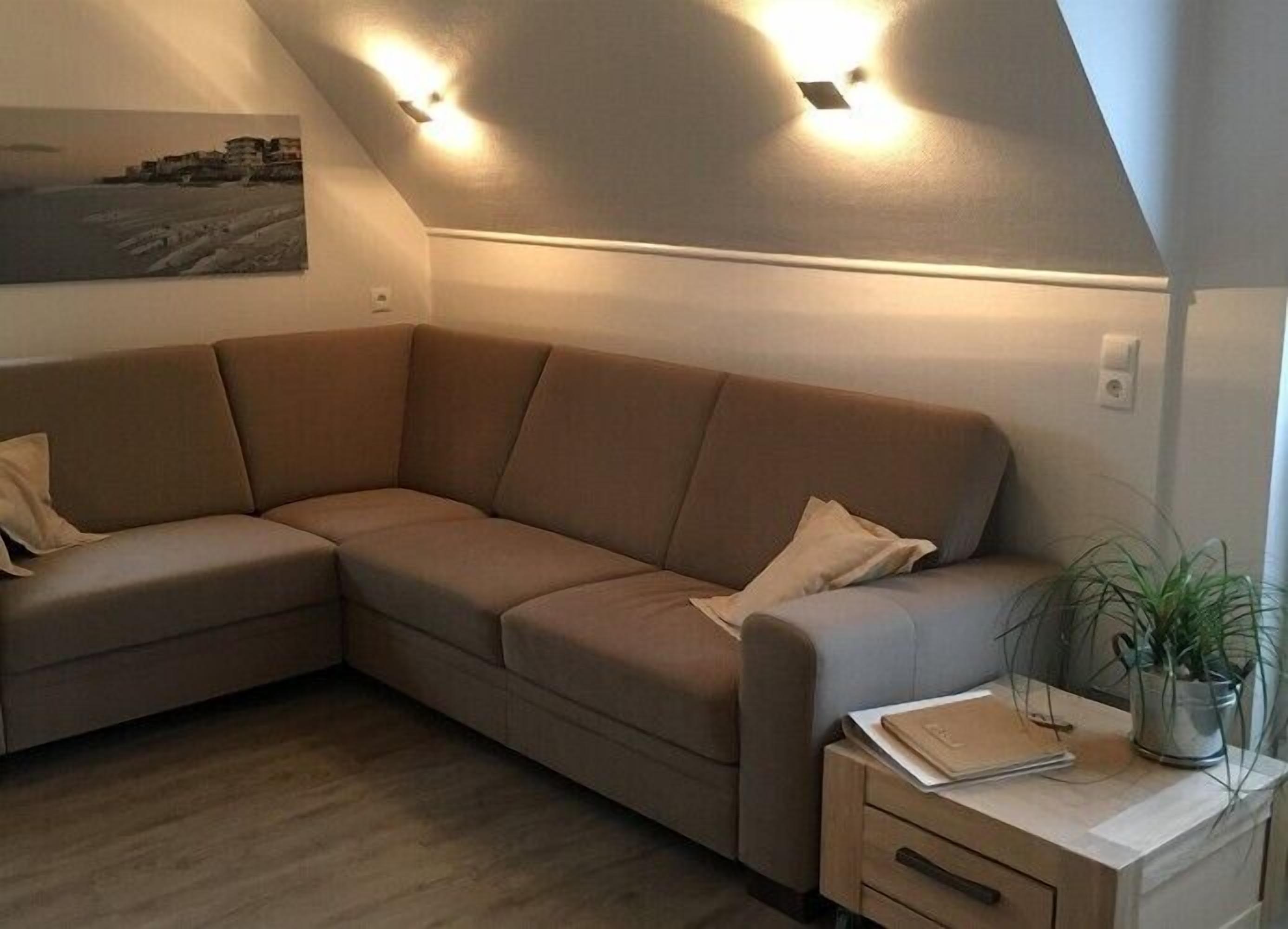 Un salón con distribución en esquina, con un sofá seccional color beige, una mesita de noche de madera y una planta en maceta.