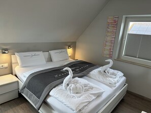 A neatly made bed with white linens, two pillows with text, a grey blanket, and two towels shaped like swans.