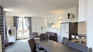 A modern kitchen with a built-in oven, a dining area with a long table and chairs, and a living area with a sofa and armchairs. - Duhner Düne apartment 25, WLAN, elevator, roof terrace, close to the beach, non-smoking (Cuxhaven)